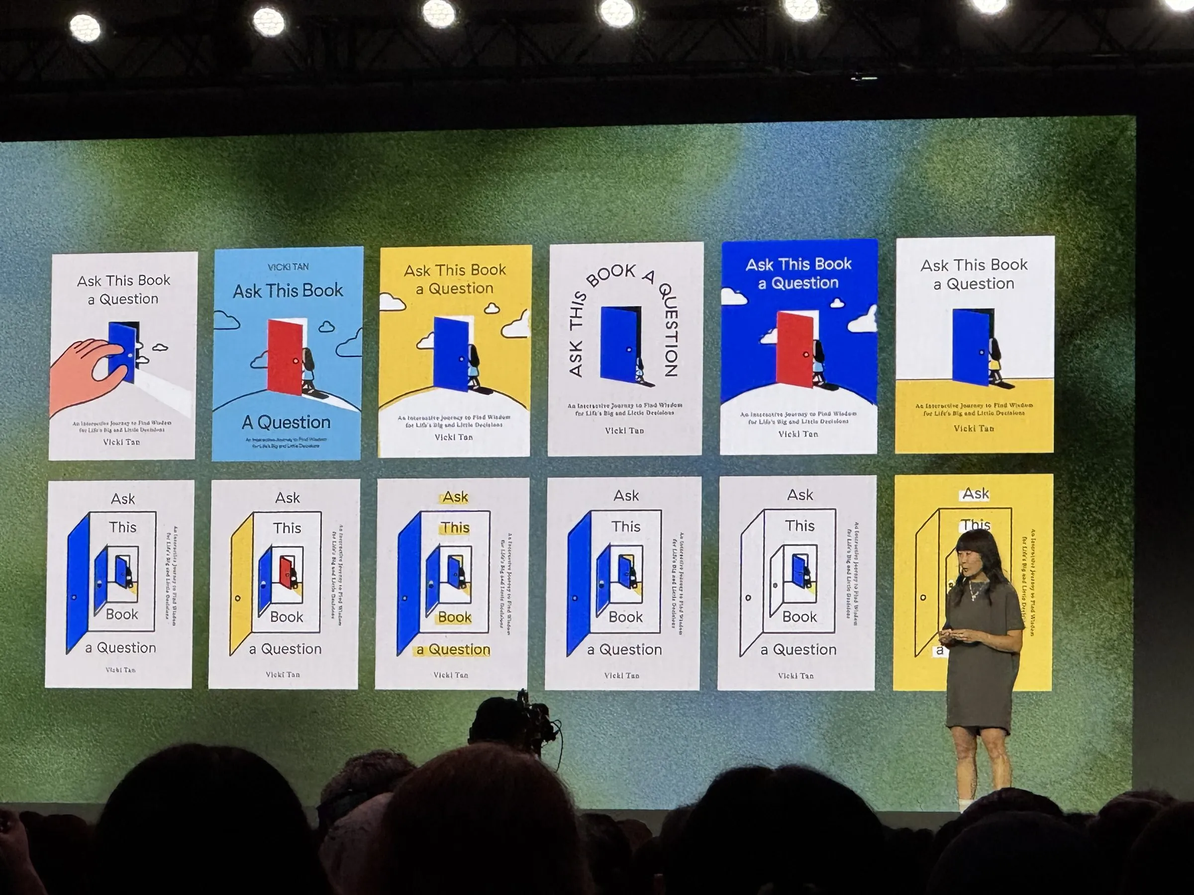Vicki Tan on stage in front of a wall of twelve cover explorations for Ask This Book a Question